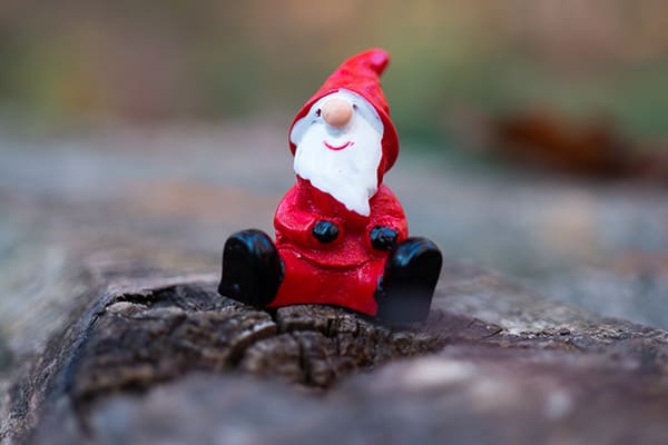 A miniature Father Christmas sitting on a tree trunk.